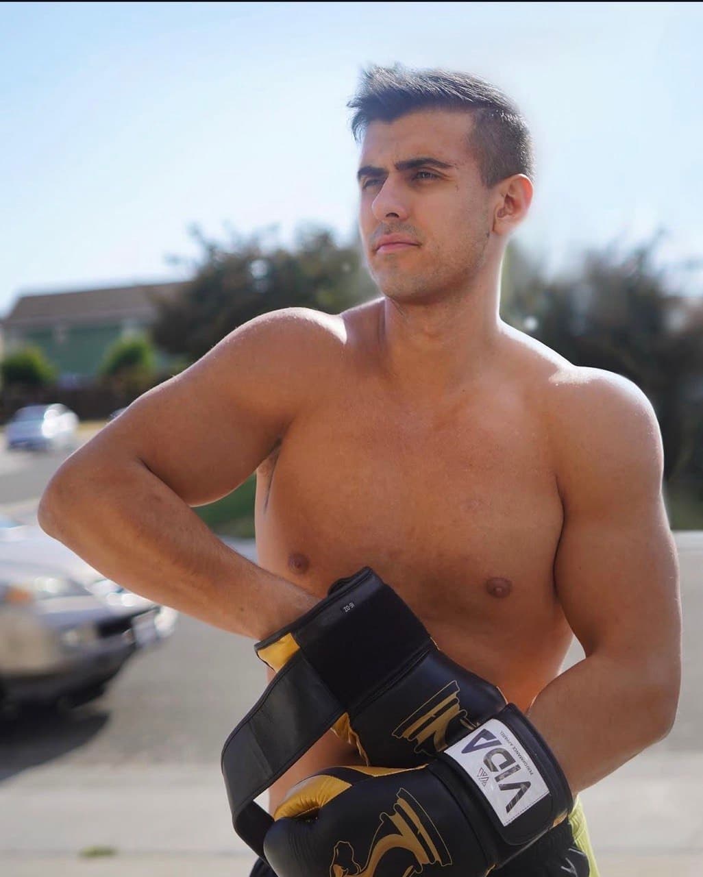 Ty shirtless in the sun, strapping on a pair of boxing gloves