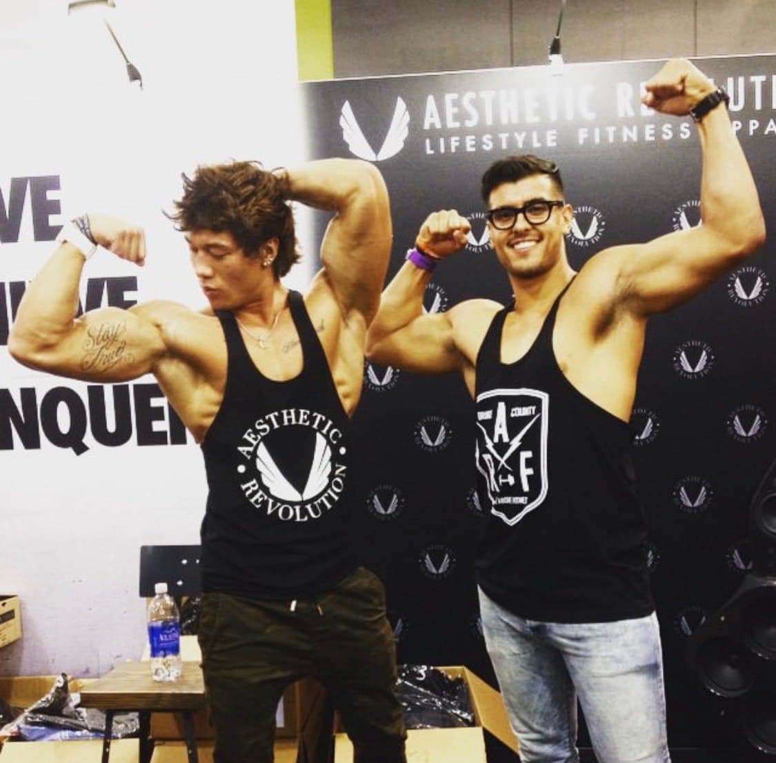 Ty flexing alongside another athlete at a fitness expo
