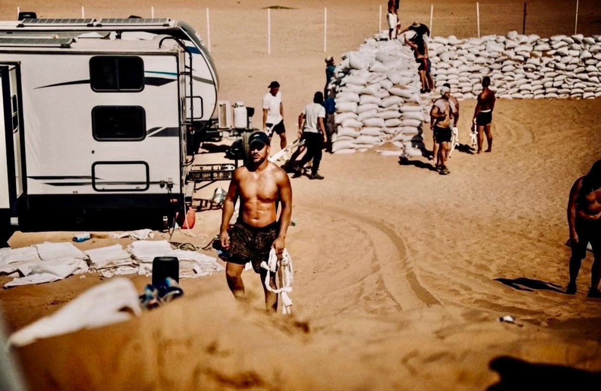 Ty crossing desert sand at a training camp, sandbags stacked behind him