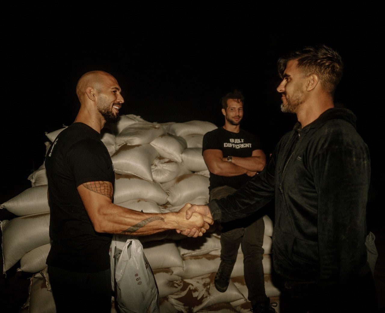 A handshake at night in front of stacked sandbags