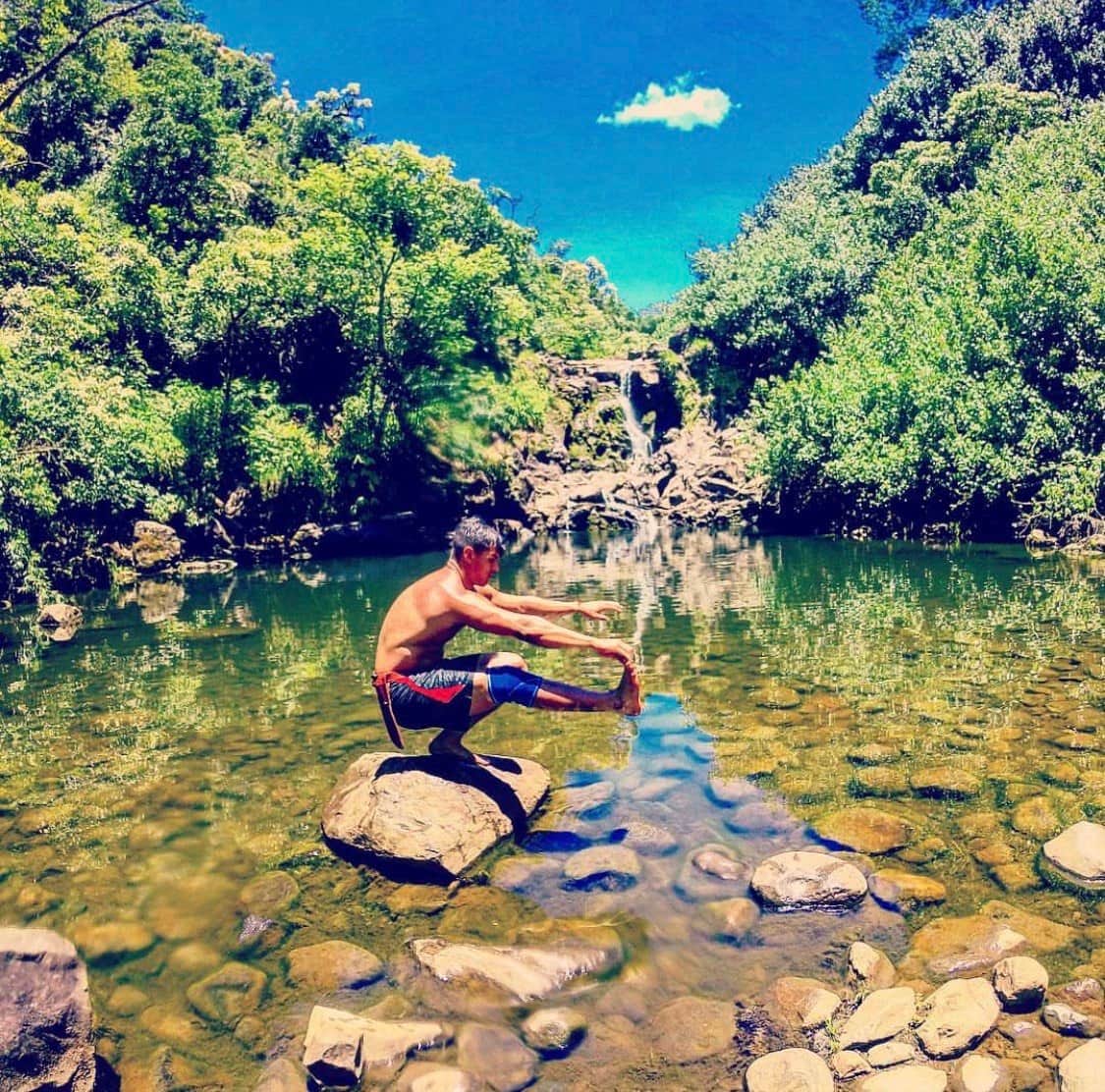 Ty balancing in a pistol squat on a rock in front of a waterfall